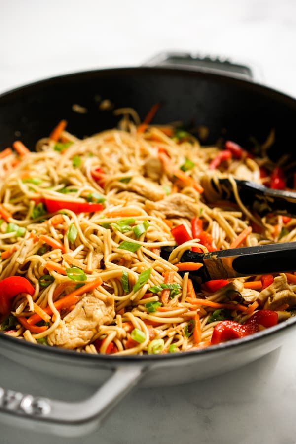 Lo Mein noodles with bell peppers, chicken and carrots in a large frying pan