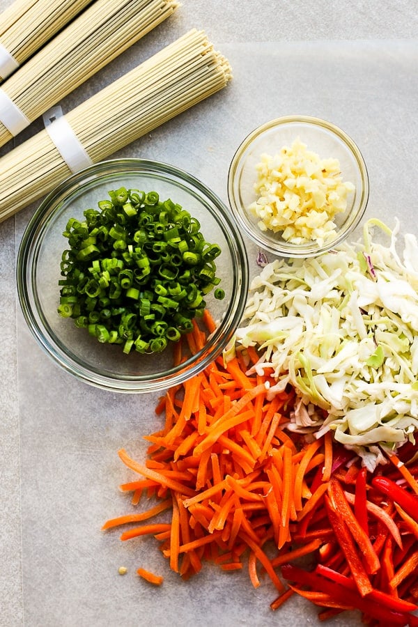 Ingredients such as noodles, shredded carrots, shredded cabbage, minced garlic, and green onions