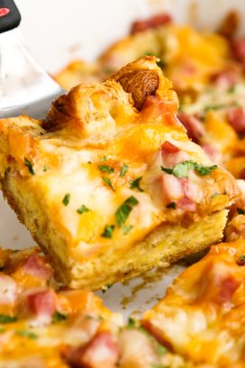Lifting up a slice of croissant bake with ham and cheese on top
