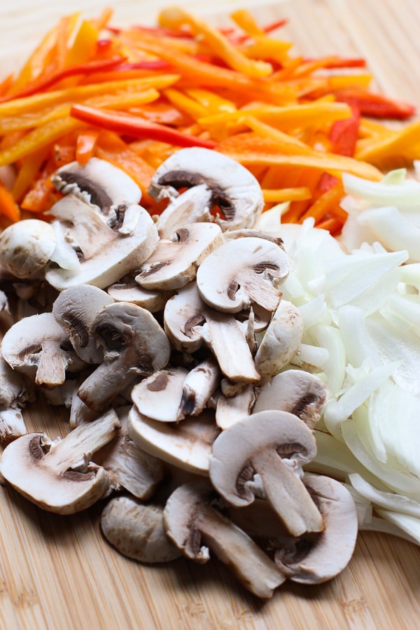 Sliced bell peppers, sliced mushrooms, slice onions on a cutting board for Slow Cooker Tomato and Herb Chicken