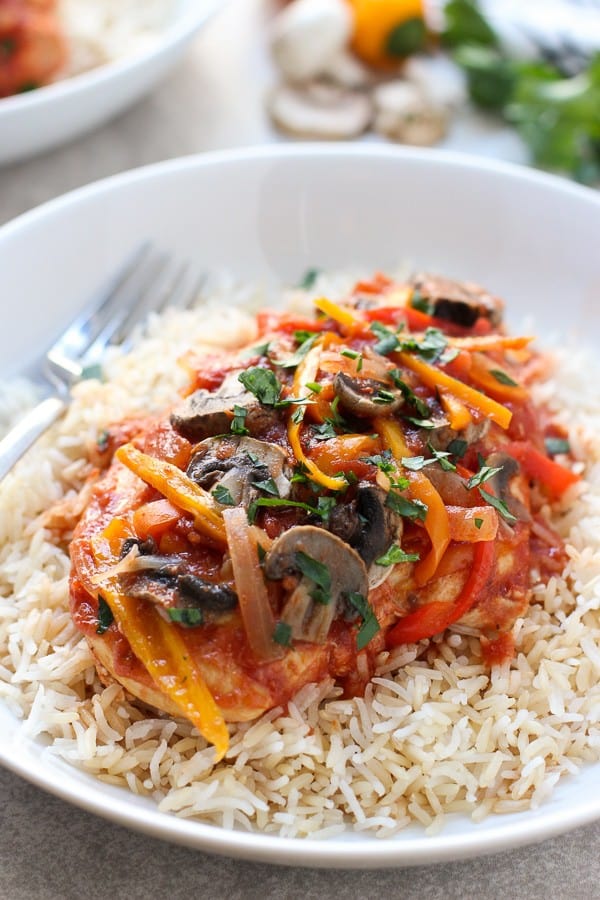 Slow Cooker Tomato and Herb Chicken with rice on a plate with a fork on the background