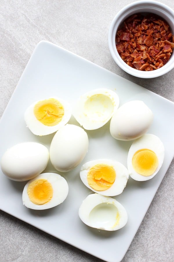 Top down shot of a plate of boiled eggs with bacon bits in the background for Bacon Deviled Eggs