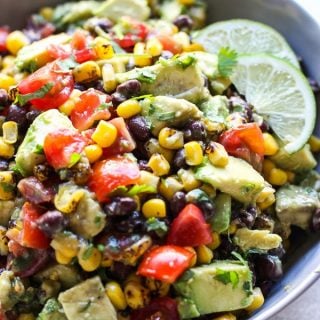 A bowl of Avocado Corn and Black Bean Salsa with lime wedges on the side