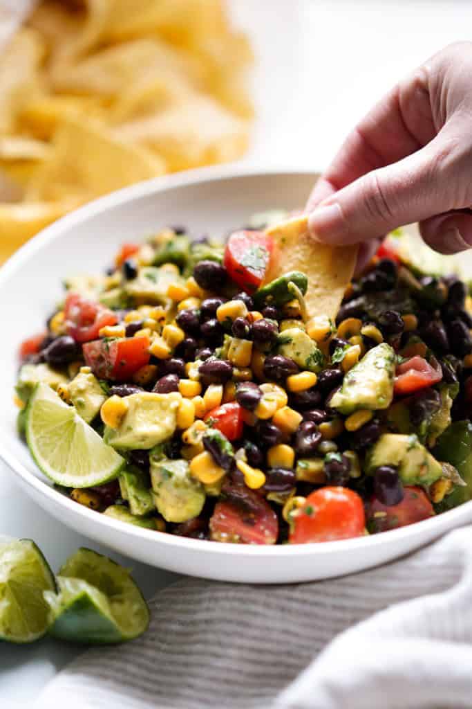 Dipping a chip into Avocado Corn and Black Bean Salsa