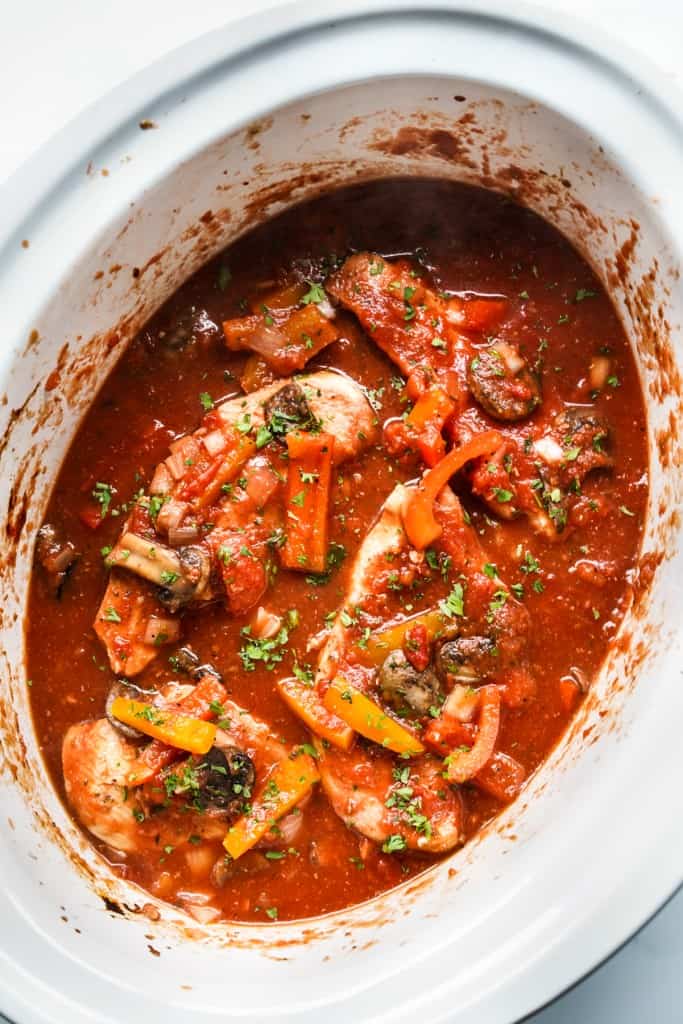 Chicken cacciatore in slow cooker, submerging in tomato based herb sauce, along with bell peppers and mushrooms