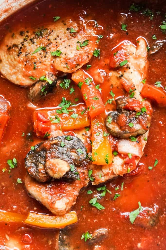 Closeup of chicken cacciatore topped with mushrooms, bell peppers and parsley