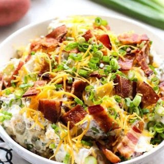 Loaded Baked Potato Salad with green onions and red potatoes behind it