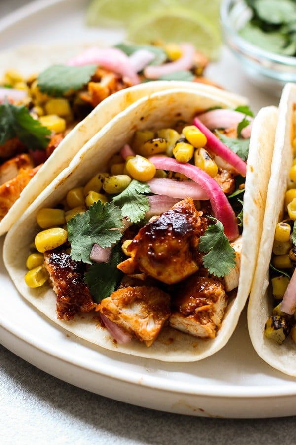 Closeup of bbq chicken wrapped in tortillas, topped with red onions, corn and cilantro