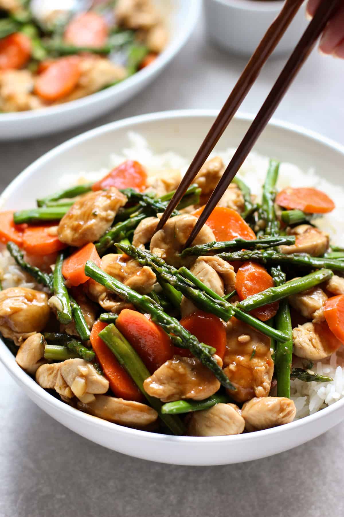 A pair of chopsticks digging into chicken and asparagus stir fry