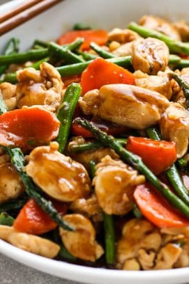 a bowl of chicken, asparagus and carrots stir fry in a sticky sauce