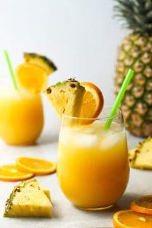 Two glasses of orange and pineapple coconut rum cocktails, with a pineapple in the background