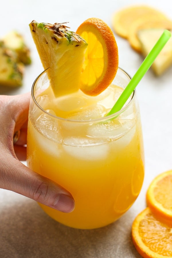 Hand holding on to a glass of Orange and Pineapple Coconut Rum Cocktail