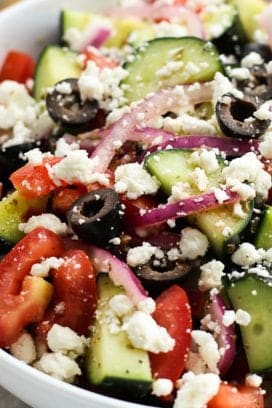a bowl of cucumber salad with tomatoes, red onions, black olives and feta cheese