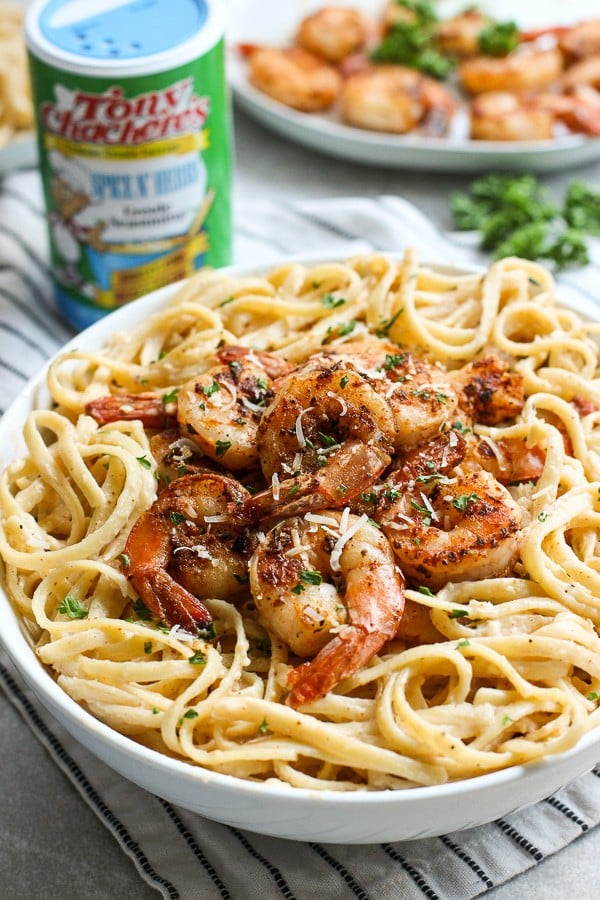 A bowl of pasta with shrimp with Tony's seasoning in the background