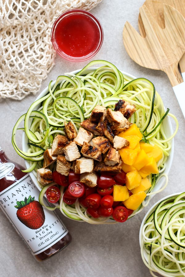 Top down view of a bowl of Grilled Chicken Zoodles with BRIANNAS blush wine vinaigrette on the side