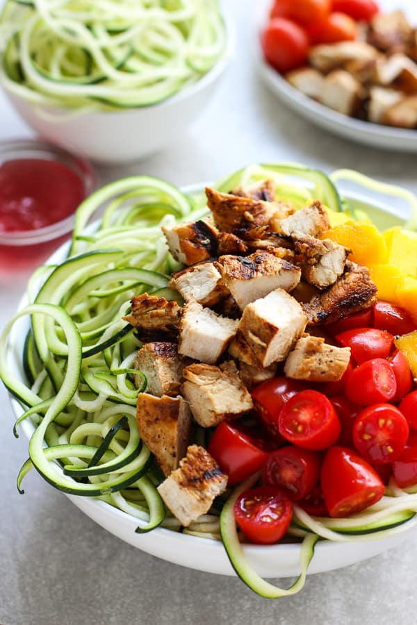 A bowl of zoodles topped with grilled chicken, mango and tomatoes