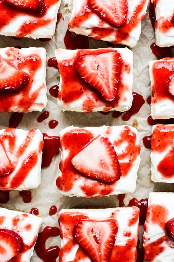 Top down view of square cheesecake bites drizzled with strawberry sauce