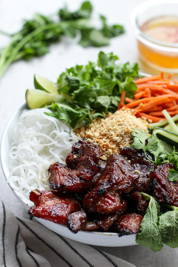 Vietnamese Noodle Bowl filled with vermicelli noodles, grilled pork and veggies, with sauce in the background