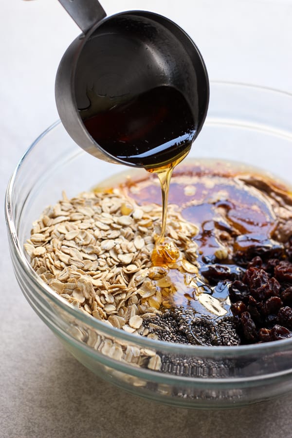 Drizzling honey into a bowl filled with oatmeal, almond butter, raisins, and chia seeds