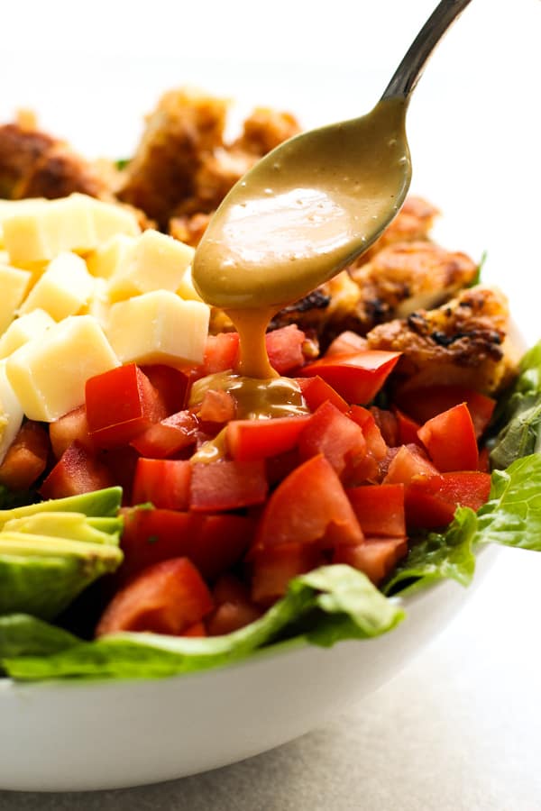 Drizzling Honey Mustard Dressing onto a bowl of Crispy Chicken Salad