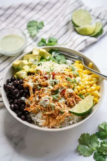 Bowl filled with chicken, corn, black beans, shredded cheese, avocados, cilantro and la wedge of lime