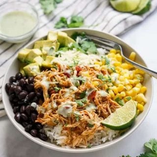 Bowl filled with chicken, corn, black beans, shredded cheese, avocados, cilantro and la wedge of lime