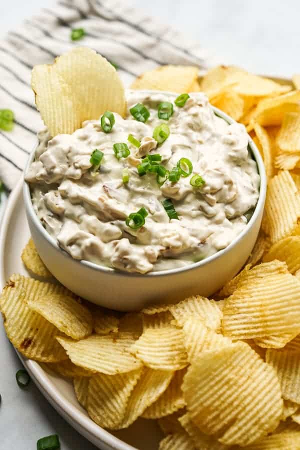 A bowl of dip with lots of potato chips around it