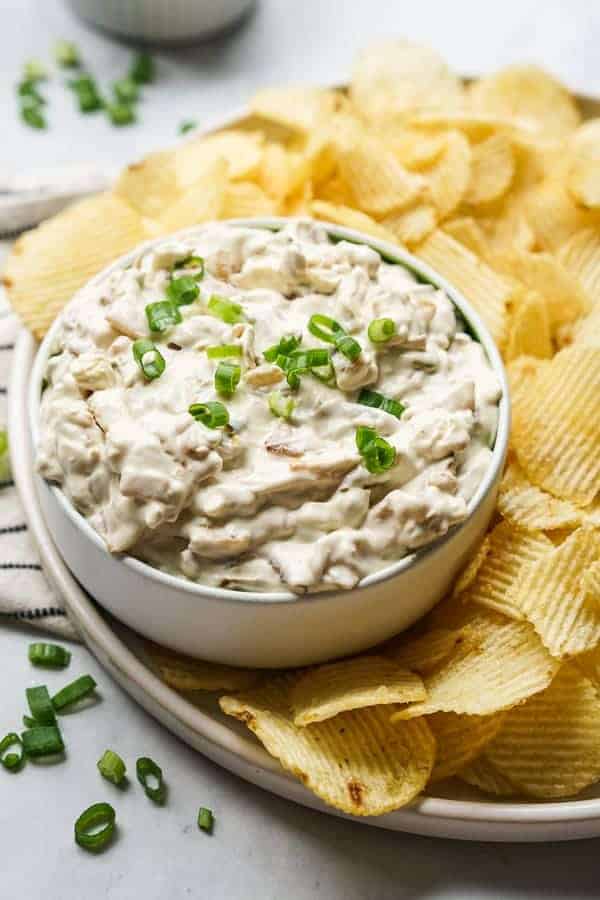 A bowl of Caramelized Onion Dip with potato chips on the side