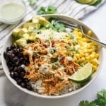 A bowl of rice, topped with shredded chicken, black beans, corn and avocado