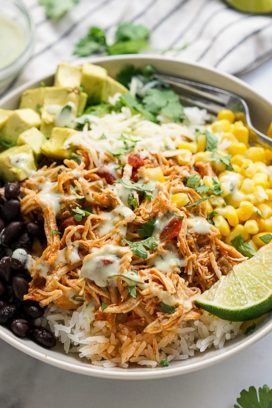 A bowl of rice, topped with shredded chicken, black beans, corn and avocado