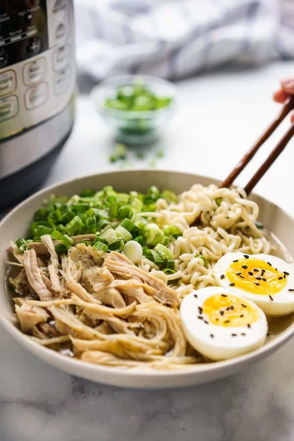 A bowl of ramen noodles with Instant Pot behind it