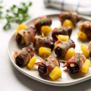 A plateful of bacon wrapped dates with a kitchen towel in the background