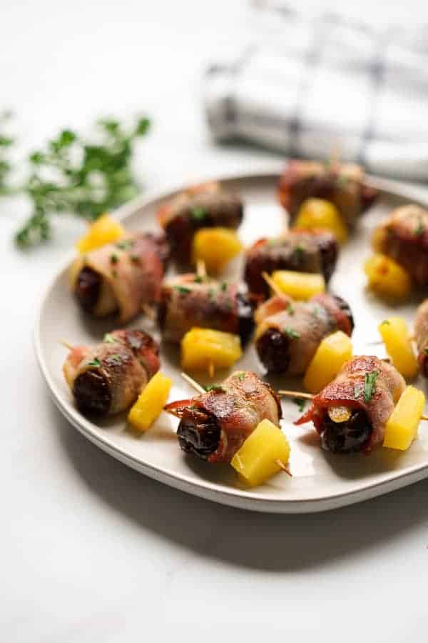A plateful of bacon wrapped dates with a kitchen towel in the background