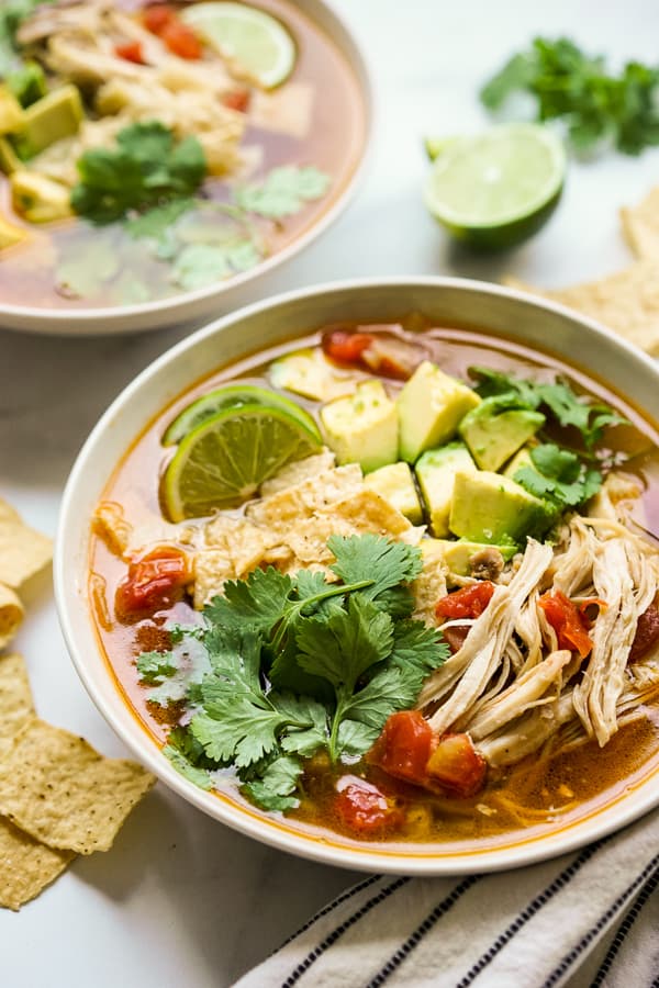 A warm bowl of Instant Pot Chicken Tortilla Soup topped with cilantro, lime and avocados