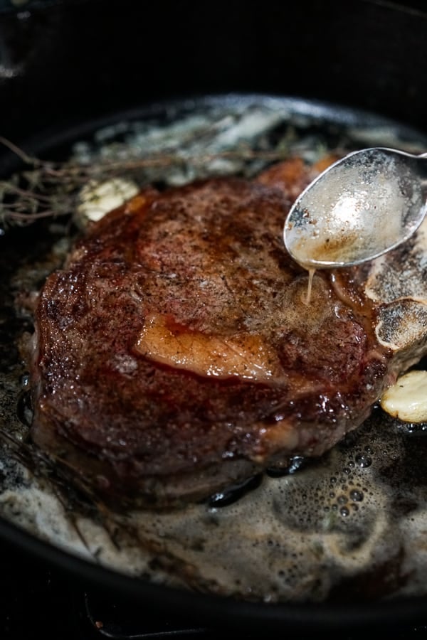 Drizzling butter over steak while searing it