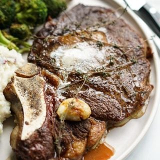 A large piece of Restaurant Style Steak with garlic, fresh thyme and butter