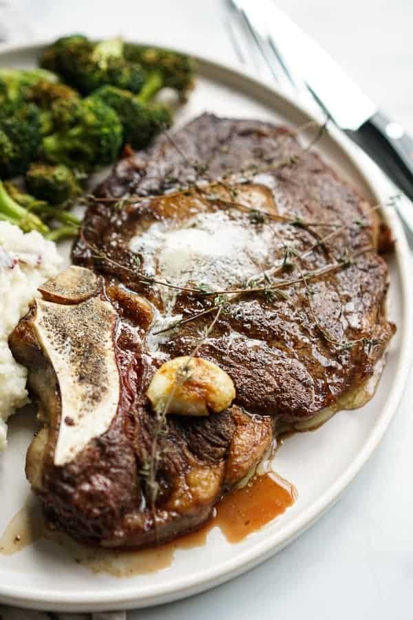 A large piece of Restaurant Style Steak with garlic, fresh thyme and butter