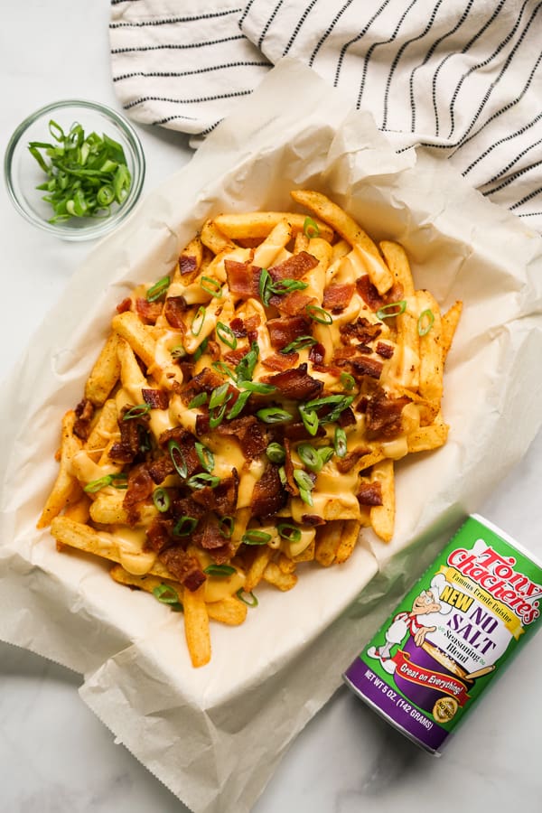 Top down view of fries with cheese sauce, bacon and green onions with seasoning next to it