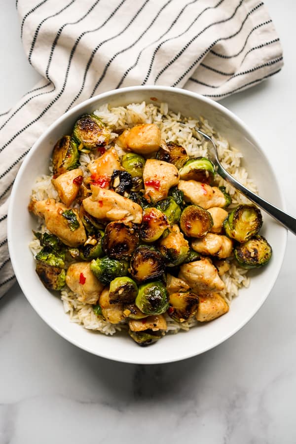 A bowl of Brussels sprouts and chicken stir fry on top of rice in a bowl with a fork