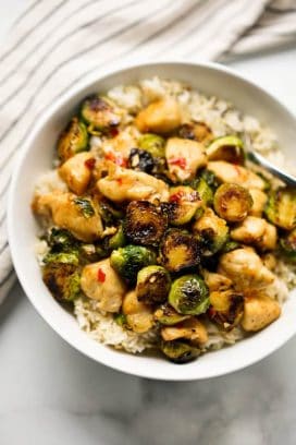 Close up of a bowl of Brussels sprouts and chicken stir fry on top of rice in a bowl