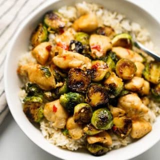 Close up of a bowl of Brussels sprouts and chicken stir fry on top of rice in a bowl