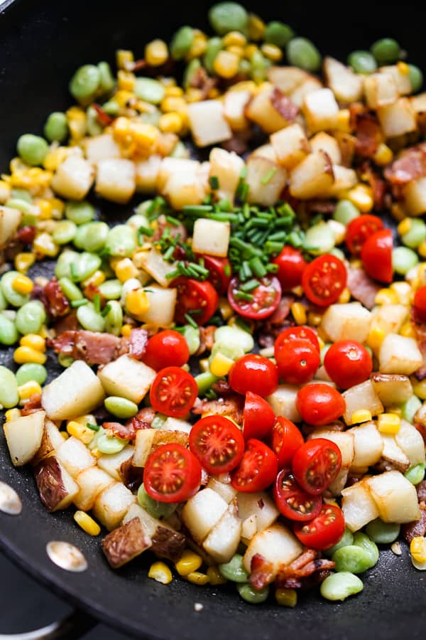 A skillet filled with potatoes, cherry tomatoes, corn and lima beans