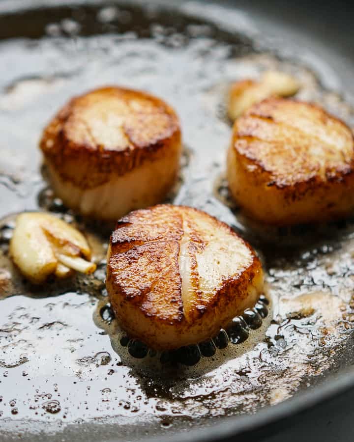 Searing scallops in butter with garlic pieces