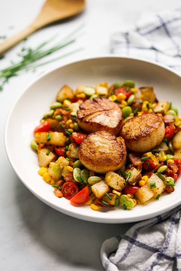 A bowl of corn, lima beans and potatoes topped with seared scallops