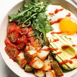 Savory breakfast bowl filled with roasted potatoes, roasted tomatoes, avocados, egg and arugula