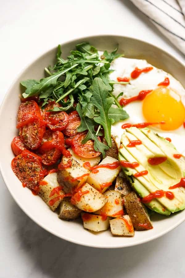 Savory breakfast bowl filled with roasted potatoes, roasted tomatoes, avocados, egg and arugula