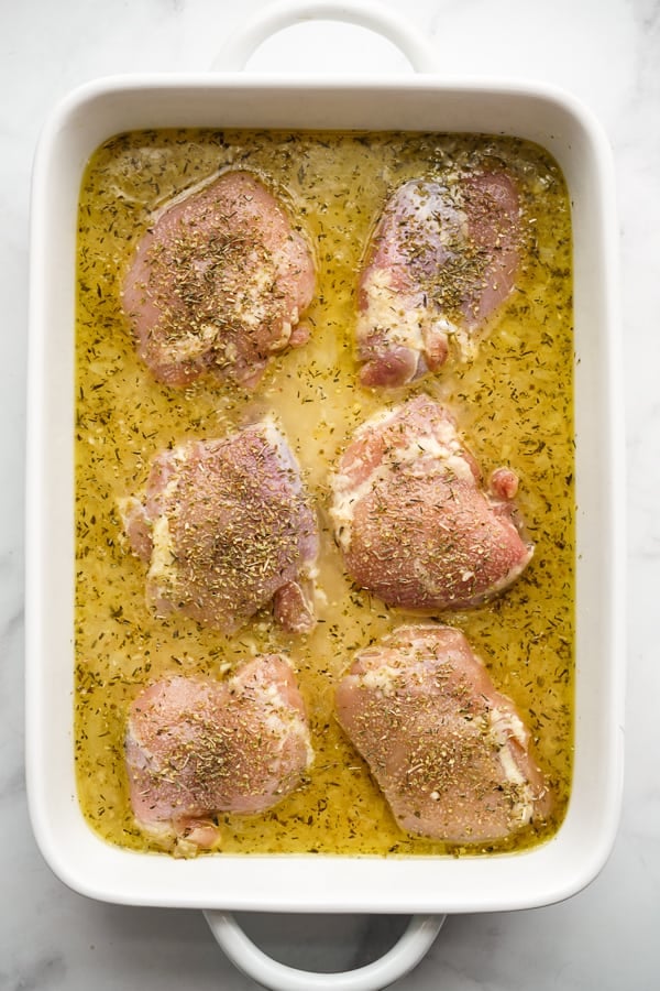 Rectangular casserole dish filled with rice, chicken stock, lemon juice, white wine and aromatics; topped with chicken thighs