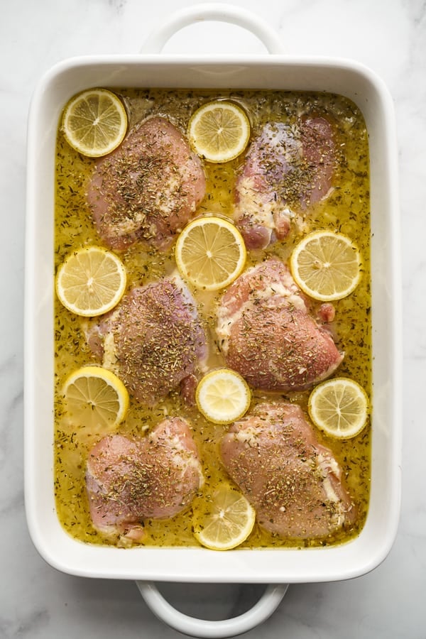 Rectangular casserole dish with rice, chicken stock, lemon juice, white wine and aromatics; topped with chicken thighs and lemons