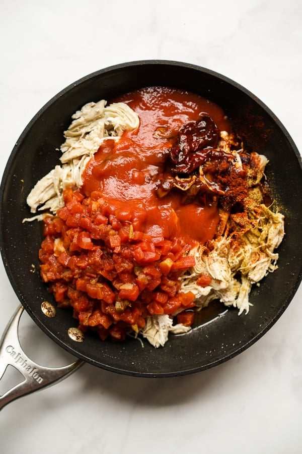 Shredded rotisserie chicken, tomatoes, chipotle peppers in adobo sauce, and spices in a skillet