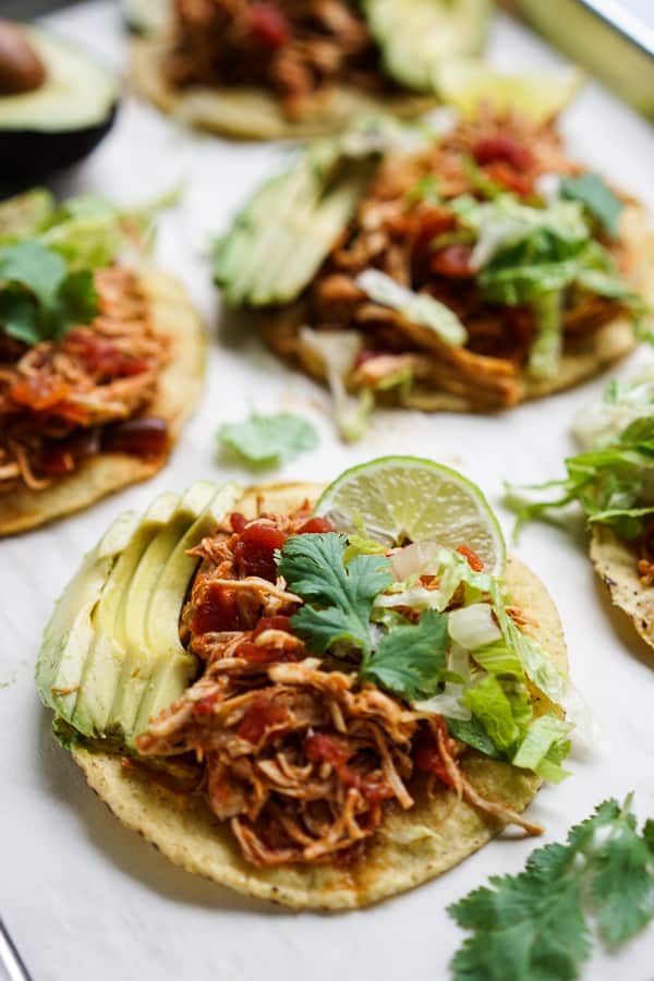 Tostadas topped with shredded chipotle chicken, avocados, cilantro, lettuce and a wedge of lime